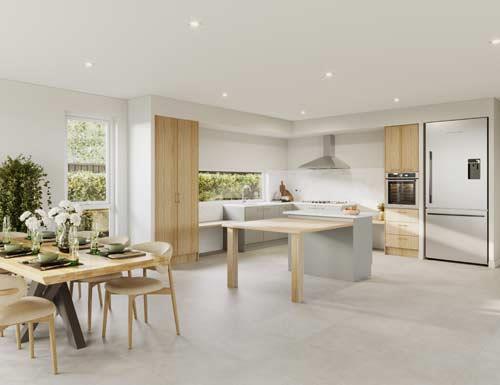 A modern, open-plan kitchen and dining area with light wood and white finishes. The kitchen features an island with a cooktop, light wood cabinets, a built-in oven, and a large refrigerator. The dining table, set for four, is positioned near a window with views of greenery outside. The space is bright with natural light and recessed ceiling lights.